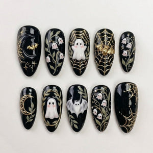 A set of ten almond-shaped press-on nails with a glossy black base. The designs feature raised 3D elements including white ghosts, gold crescent moons, gold spider webs, gold bats, and delicate white lily of the valley floral motifs.