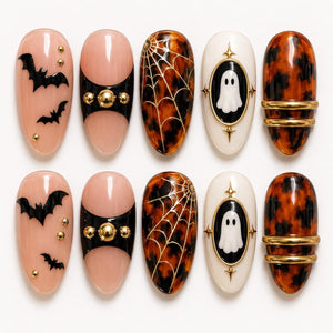 A set of ten press-on nails featuring Halloween designs. The nails include light pink bases with black bat silhouettes and gold studs, black accents with gold spheres, brown tortoiseshell patterns with gold spiderwebs, white ovals with ghost illustra