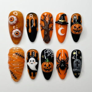 A set of ten almond-shaped press-on nails featuring Halloween designs in orange, black, and white. The set includes 3D elements like eyeballs, a tree, a witch hat, a pumpkin, a mummy wrap, a ghost, a spider, and a tombstone.