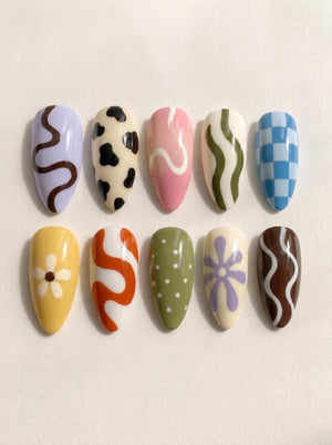 Ten almond-shaped press-on nails featuring various designs: a lavender nail with a brown squiggle, a cream nail with black cow spots, a pink nail with a white swirl, a cream nail with green waves, and a blue and white checkered nail.