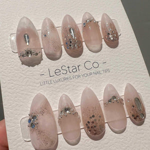 A set of ten almond-shaped press-on nails in a pale pink hue, featuring silver glitter accents and clear rhinestones. The nails are displayed on a white card labeled LeStar Co - LITTLE LUXURIES FOR YO