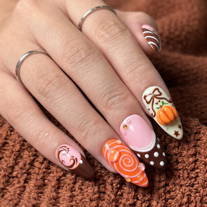 Handmade autumn press on nails with black cat, orange pumpkin, fall leaf and swirl designs in blush pink, brown, black and orange almond shapes.