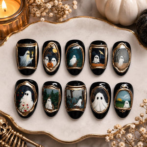 A set of ten black press-on nails, each featuring a unique hand-painted ghost scene framed in metallic gold. The designs include ghosts in forests, graveyards, and with pumpkins, all rendered in detailed miniature art on an oval nail shape.