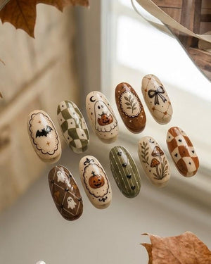 A set of ten oval-shaped press-on nails featuring various autumn and Halloween designs, including a black bat, green checkered pattern, a ghost holding a pumpkin, a botanical frame, a black bow, mushrooms, and brown checkered patterns.