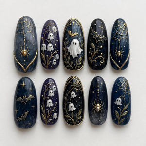 A set of ten almond-shaped press-on nails featuring dark blue and black marble backgrounds. Designs include raised white ghosts, gold metallic spider webs with spiders, lily of the valley flowers, and flying bats with gold accents.