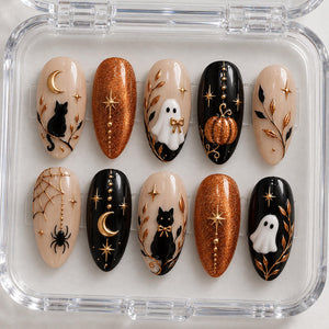 A set of ten almond-shaped press-on nails in a clear plastic case, featuring Halloween-themed designs including black cats, white ghosts, orange glitter, gold moons, stars, spiderwebs, spiders, pumpkins, and gold leaf branch accents.