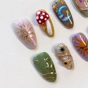 A set of six almond-shaped press-on nails featuring diverse designs including a gold sun on a pearlescent base, a red mushroom, a blue crescent moon, a green swirl pattern, two realistic eyes, and an orange sun with a face.