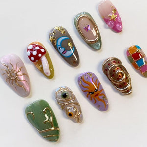 A collection of ten almond-shaped press-on nails featuring diverse designs including a red mushroom, a blue crescent moon, a gold sun, a purple sun, a green leaf pattern, a pink gradient with stars, and various gold metallic accents.