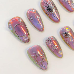 A set of almond-shaped press-on nails featuring a pearlescent purple and pink iridescent finish. Each nail is decorated with raised silver metallic celestial motifs including suns, moons, stars, and planets, accented with small clear beads.