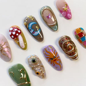 A collection of ten almond-shaped press-on nails featuring diverse designs including a red mushroom, a blue crescent moon, a purple sun, gold foil accents, a butterfly, a spiral metallic texture, and colorful geometric patterns.