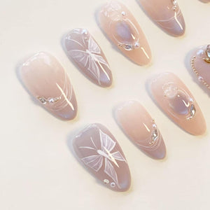A set of almond-shaped press-on nails featuring a soft nude gradient base. The designs include hand-painted white butterfly wings, delicate pearl accents, and small clear rhinestones arranged on the smooth, glossy surface of each nail.