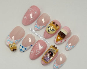 A set of artificial nails with various designs. Some nails are pink with white star patterns, others have a pink and blue plaid design. Several nails feature 3D embellishments, including a dog, an ice