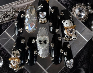 A set of ten press-on nails featuring a glossy black finish, accented with silver glitter, clear rhinestones, white pearls, and three-dimensional charms including a white bear, a metallic bear, and he