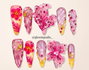 A set of ten press-on nails featuring a tropical theme with pink, purple, and yellow gradients. The nails are decorated with 3D floral designs, metallic gold starfish, seashells, pearls, and pink rhin