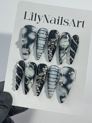Set of ten black and white press-on nails with silver accents. The nails feature different designs, including swirls, stripes, and a cross.