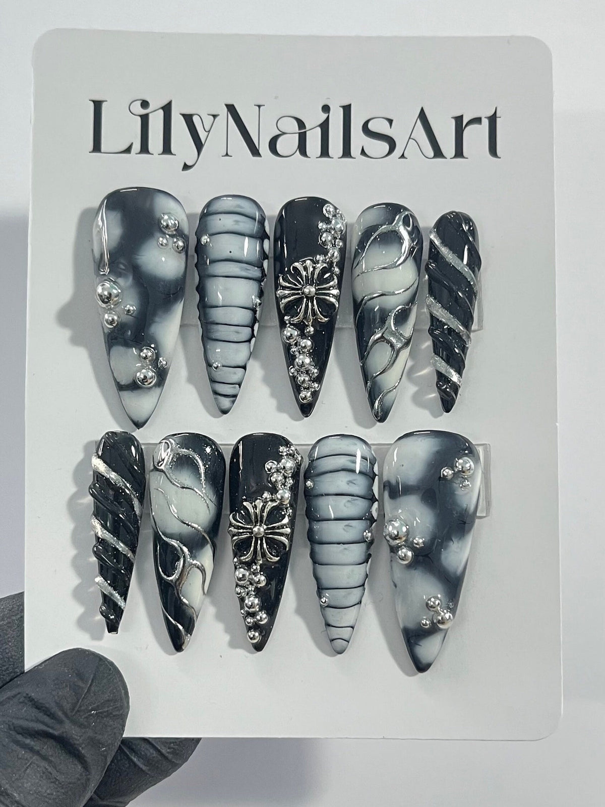 Set of ten black and white press-on nails with silver accents. The nails feature different designs, including swirls, stripes, and a cross.