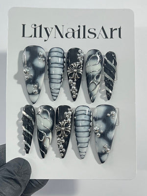 Set of ten black and white press-on nails with silver accents. The nails feature different designs, including swirls, stripes, and a cross.