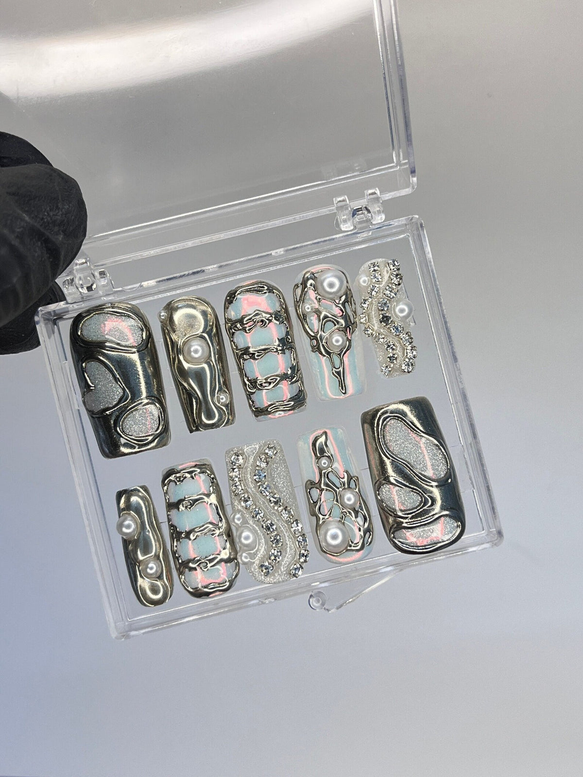 A set of ten false nails with a variety of designs. The nails are in a clear plastic case. The designs include silver swirls, white stripes, and pearl accents.