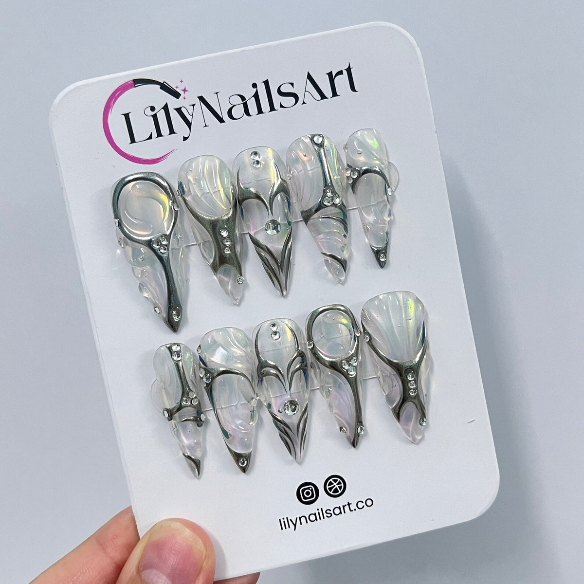 Set of ten white and silver press-on nails with a decorative design. The nails are arranged in two rows on a white card with the text "LilyNailsArt" and "lilynailsart.co".