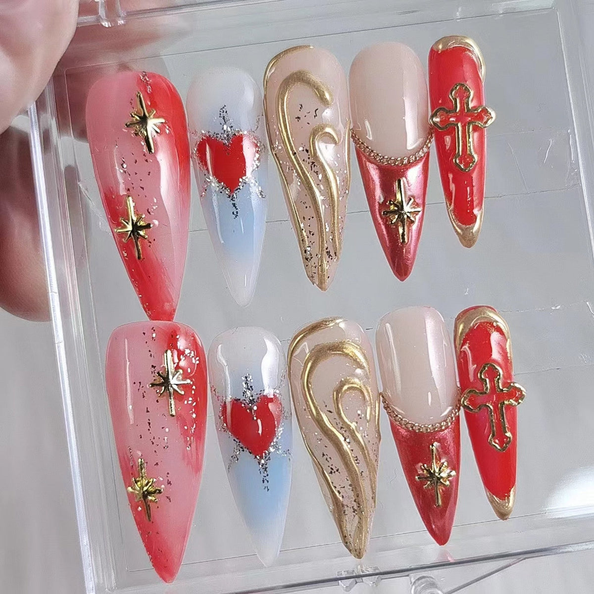 Set of ten false nails with various designs.  The designs include a red heart, a gold swirl, a red cross, and a gold star.  The nails are in a clear plastic box.
