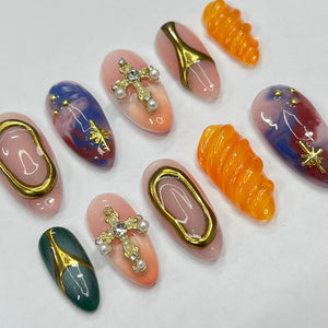 Set of ten false nails with various designs. Some nails feature a swirl pattern, others have a cross design with rhinestones, and some have a blue and white marbled design.
