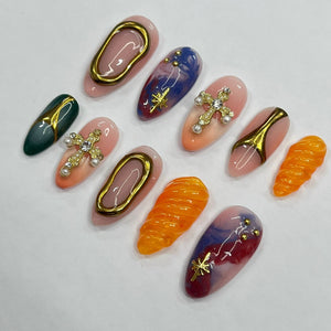Set of ten false fingernails with various designs. The designs include a swirl pattern in blue and white, a cross with rhinestones, a swirl pattern in pink and white, a seashell design, a green and go