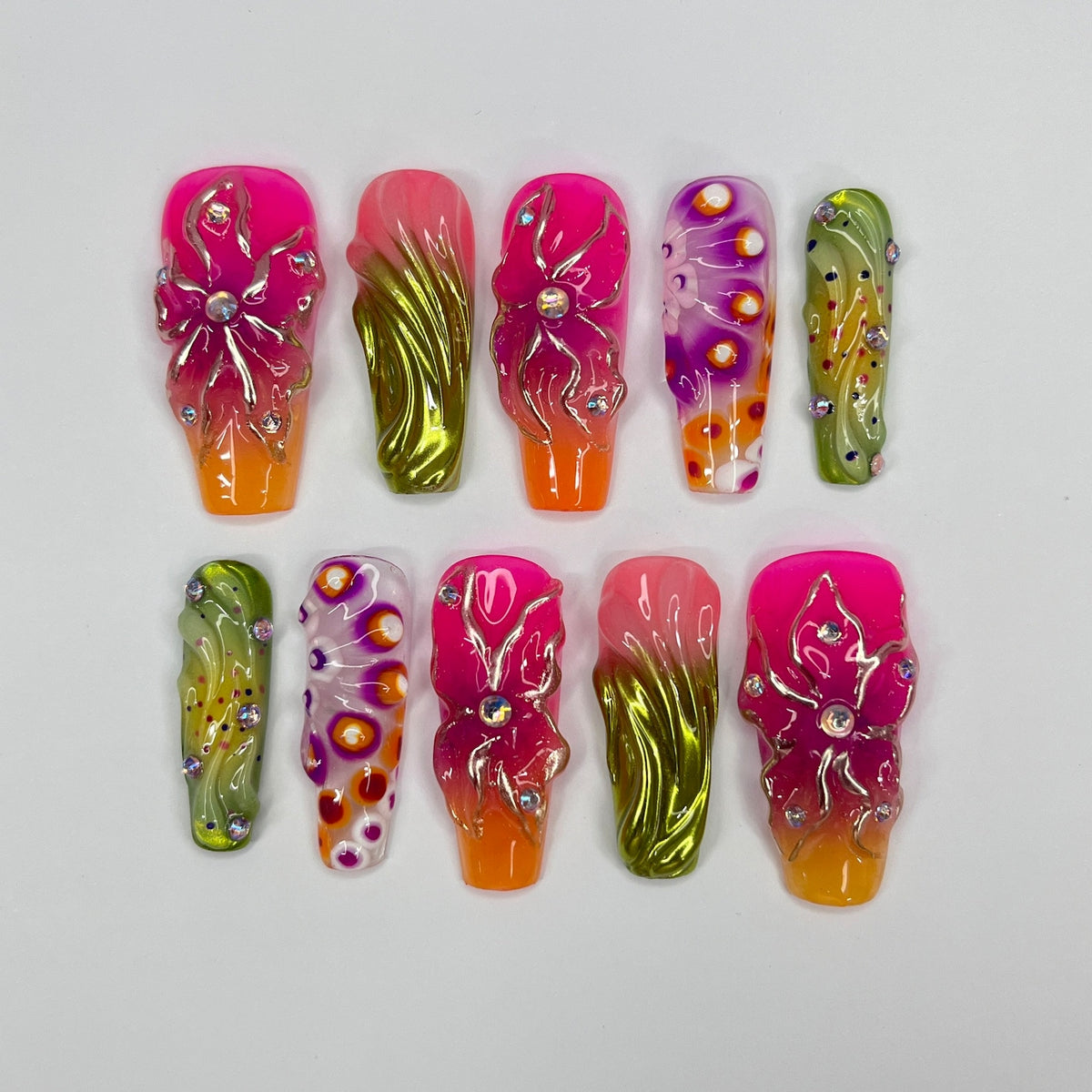 Ten long, pink, and green artificial nails with floral designs. Each nail has a different design featuring flowers, swirls, and glitter.