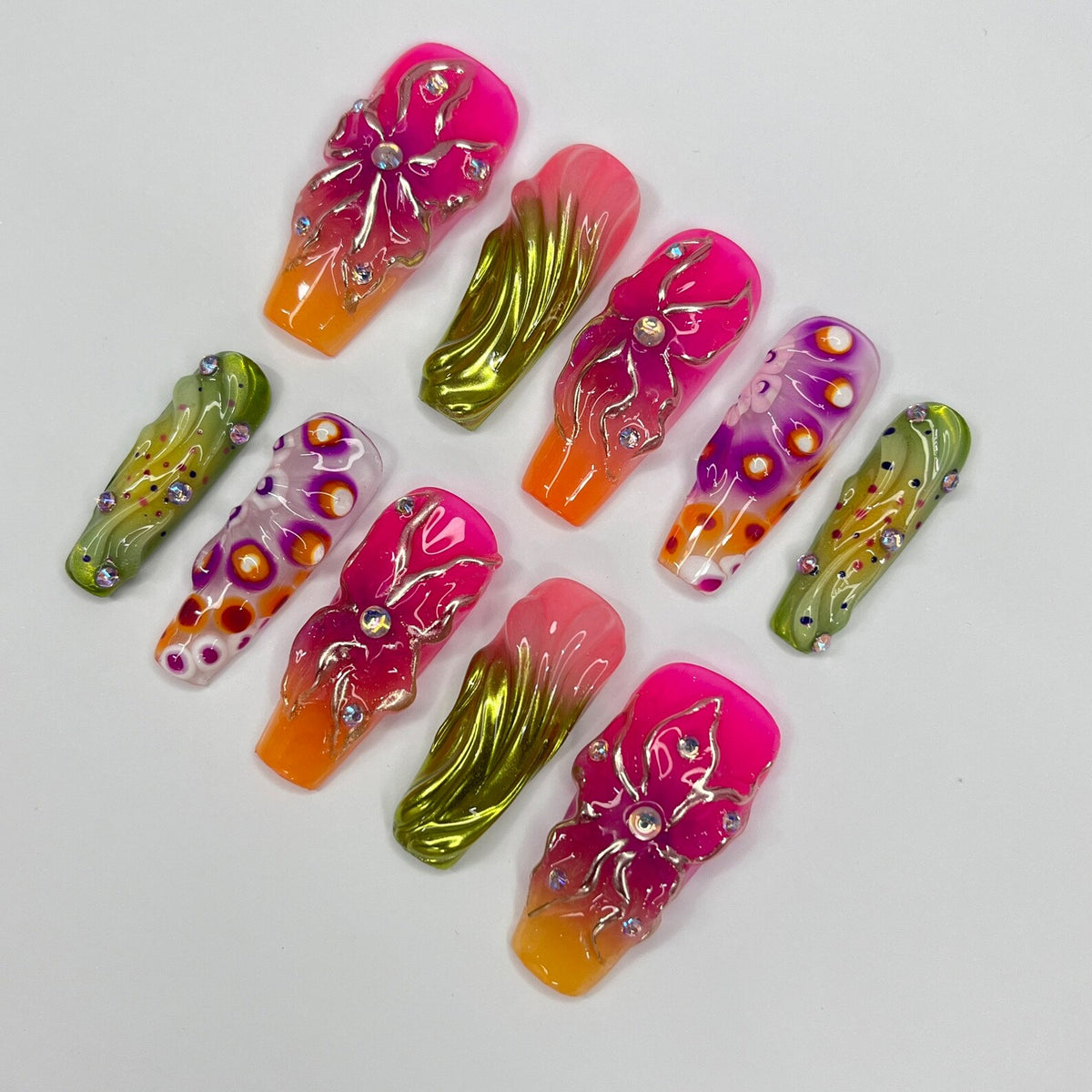 Set of ten false nails with various designs. The nails are decorated with pink, green, and orange colors, and feature swirls, flowers, and dots. Some nails have rhinestones.