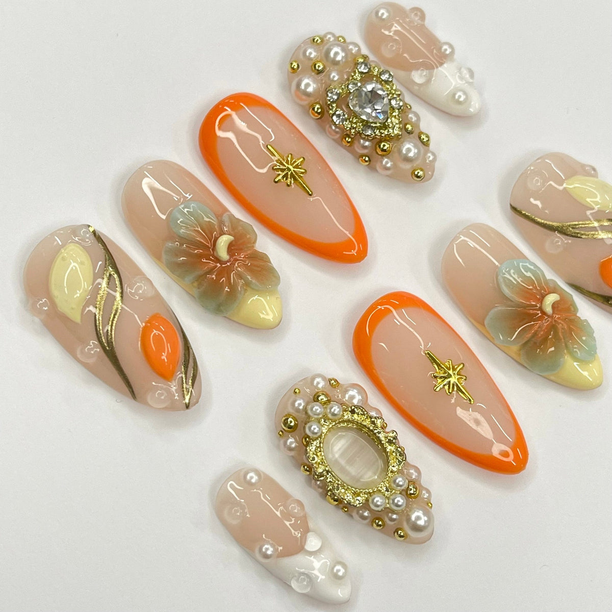 Set of ten peach-colored press-on nails with various designs. Some nails feature gold accents, pearl embellishments, and floral designs.