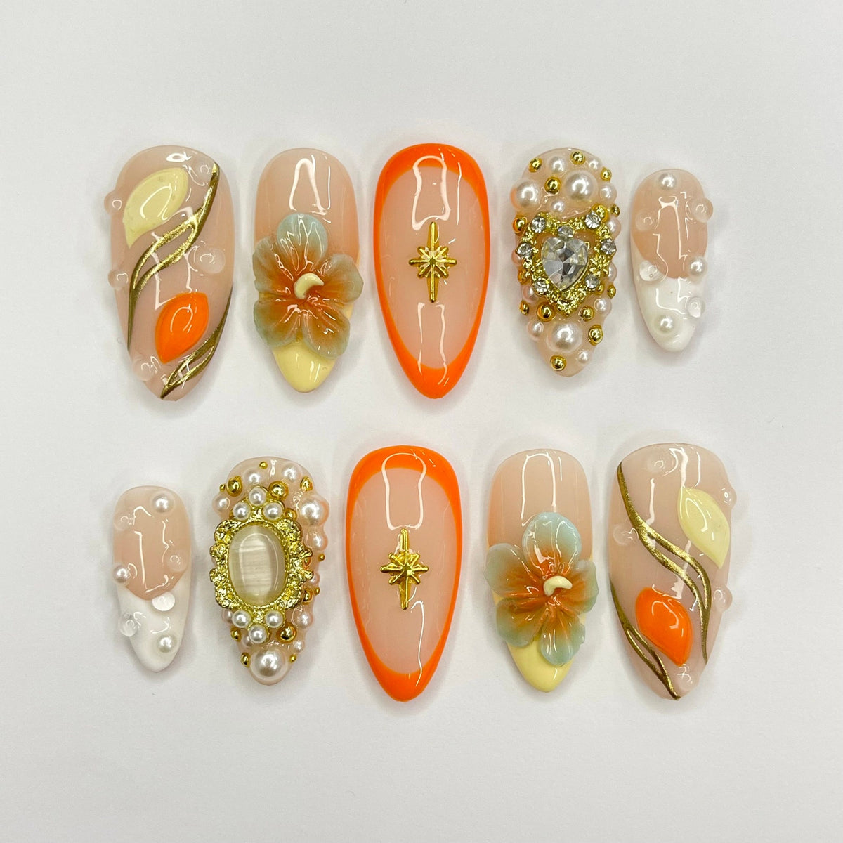 Eight peach-colored nail tips with various designs. The designs include a flower, a star, a heart, and a swirl pattern. The nail tips are decorated with gold and white accents.