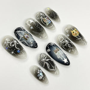 Set of ten black and white ombre nail tips with silver glitter and cat illustrations.