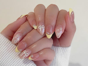 Close-up of hands with light pink nail polish and yellow tips. Some nails have white bows painted on them.