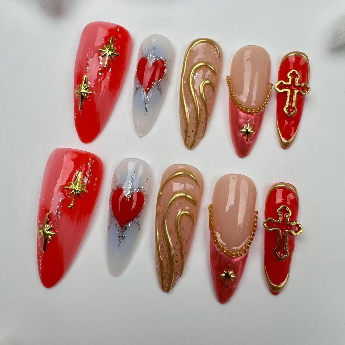 Set of ten red, white, and gold press-on nails with various designs, including hearts, crosses, and swirls.