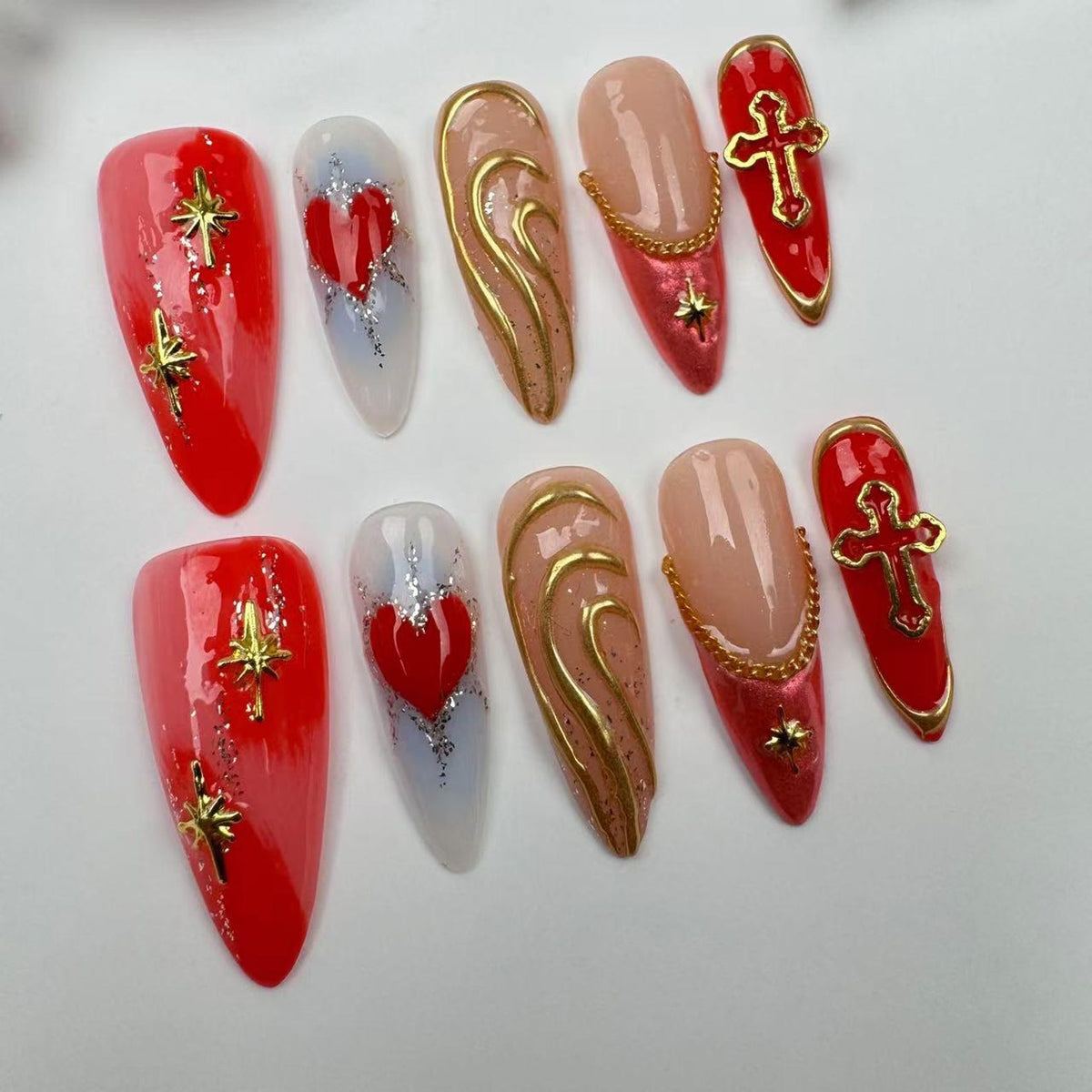 Set of ten false nails with different designs. The designs include a red heart, a gold swirl, a cross, and a star. The nails are all long and pointed.