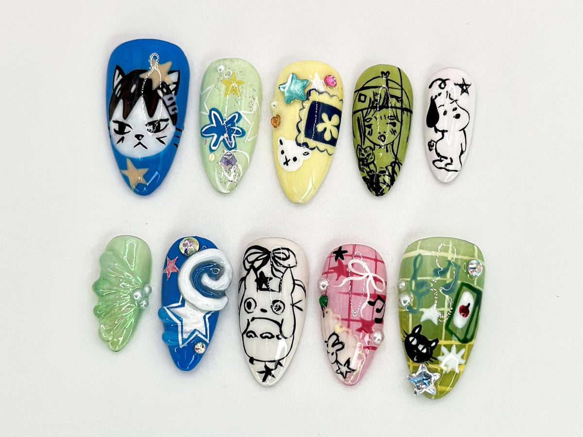 Ten different nail designs featuring various cartoon characters and patterns. The designs include a cat, a flower, a cartoon character with a hat, a dog, a butterfly, a spiral, a cartoon character with a bow, a checkered pattern, a green cat, and a b
