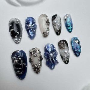 Ten different nail designs featuring blue, white, and silver accents. Some designs include flowers, crosses, and pearls.