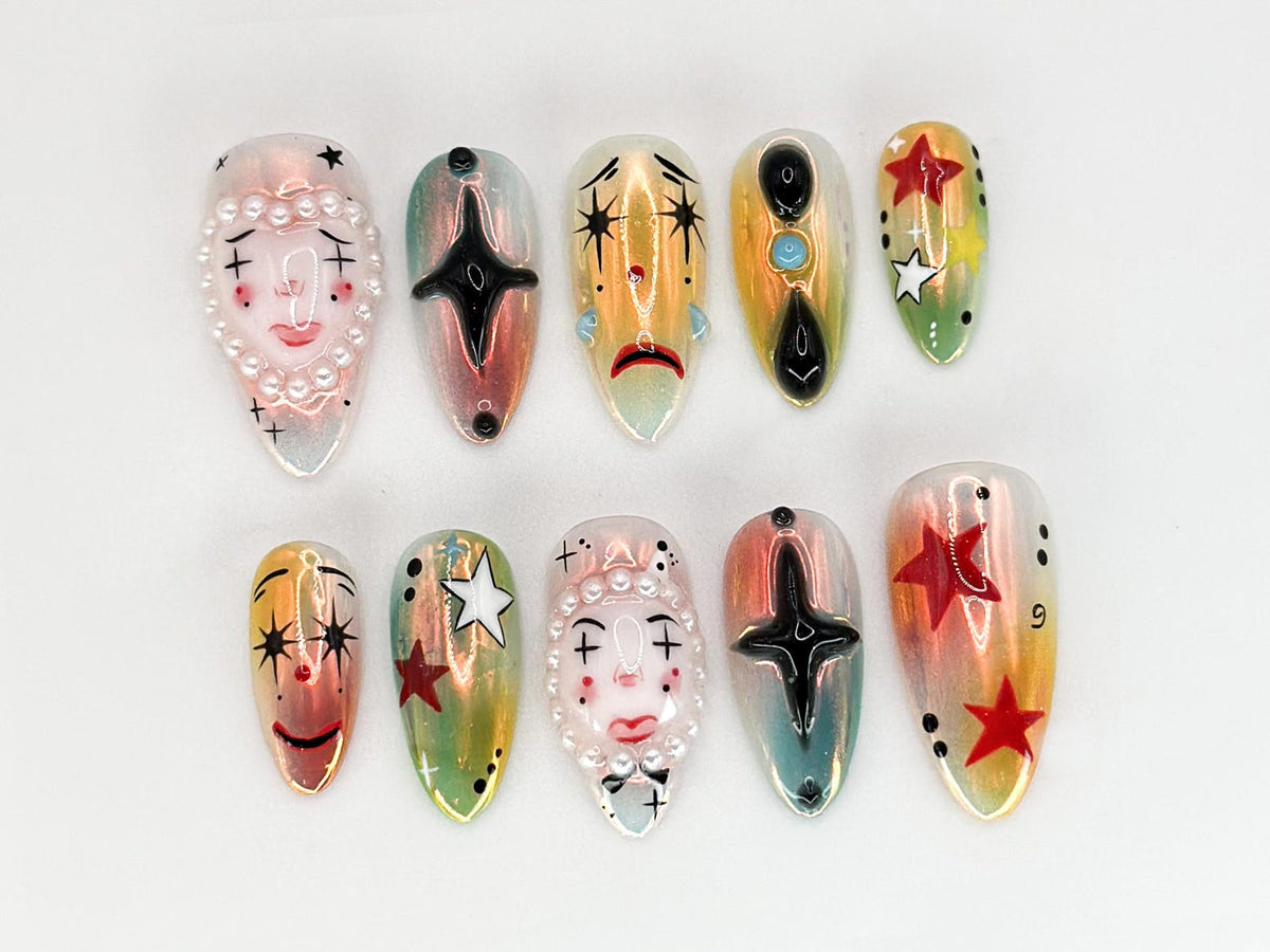Set of ten false nails with various designs. The nails are iridescent and feature painted designs of stars, faces, and abstract shapes.