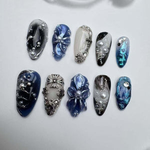 Ten blue and white nail tips with various designs, including flowers, swirls, and a cross. Some tips have pearl accents.
