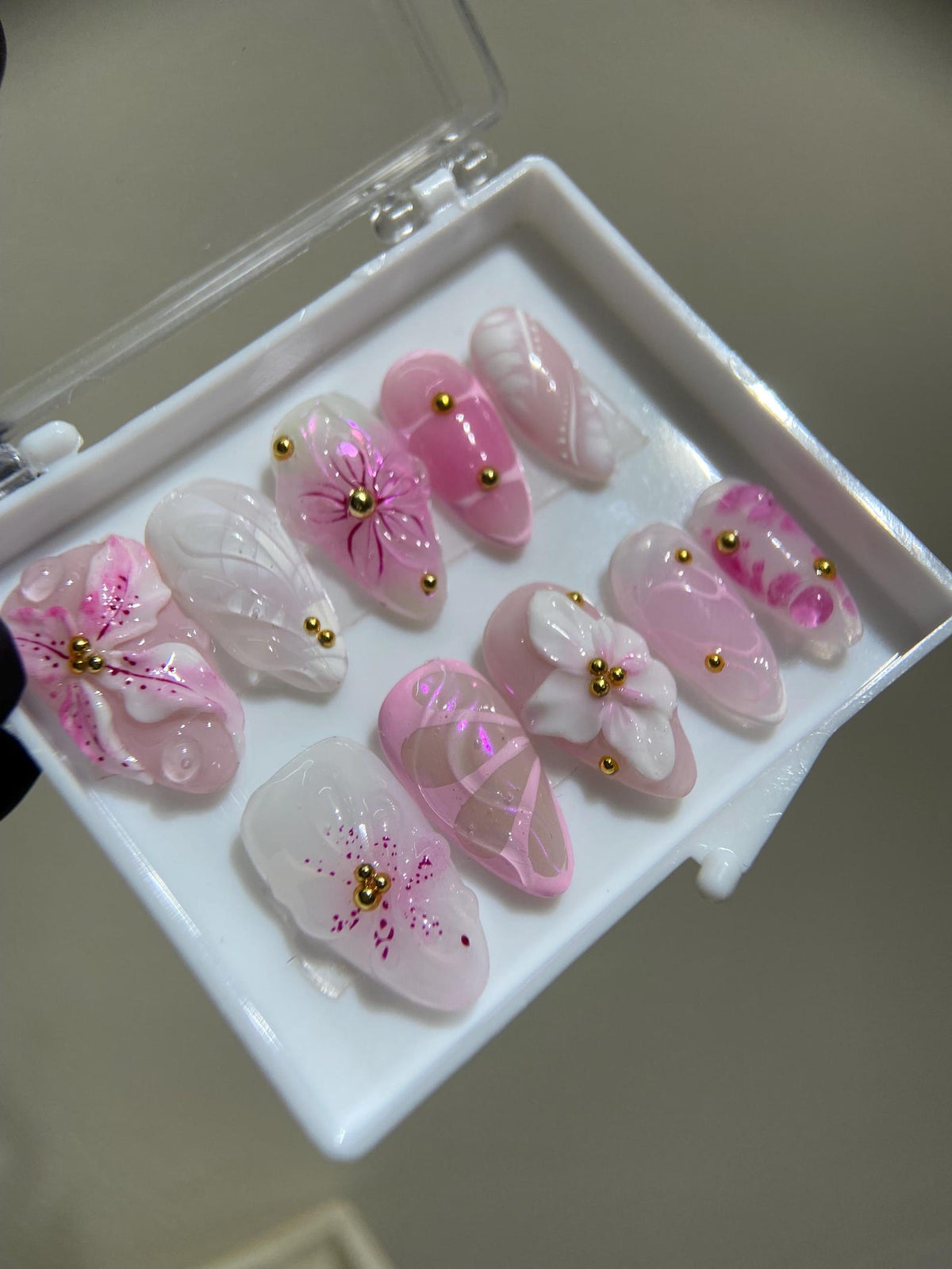 A set of ten pink and white false nails with floral and other designs. The nails are arranged in a white box.
