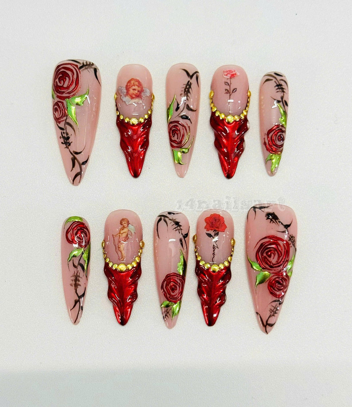 Set of ten long, stiletto-shaped false nails with a pink base and various designs. Some nails feature red roses, a cherub, and gold accents. Others have a red base with gold accents.