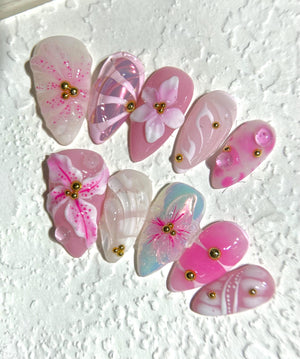 Set of ten pink and white false nails with floral designs and gold accents.