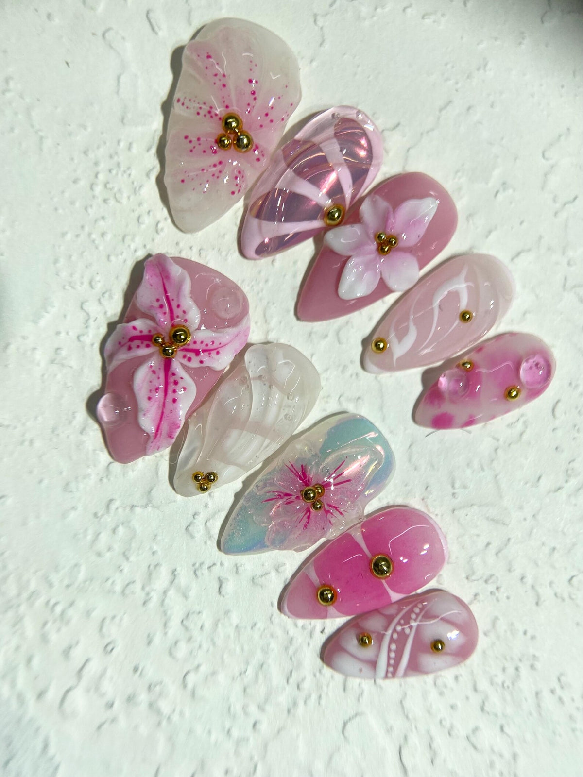 Set of ten pink and white false nails with floral designs and gold accents.