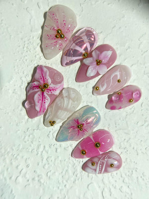Set of ten pink and white false nails with floral designs and gold accents.
