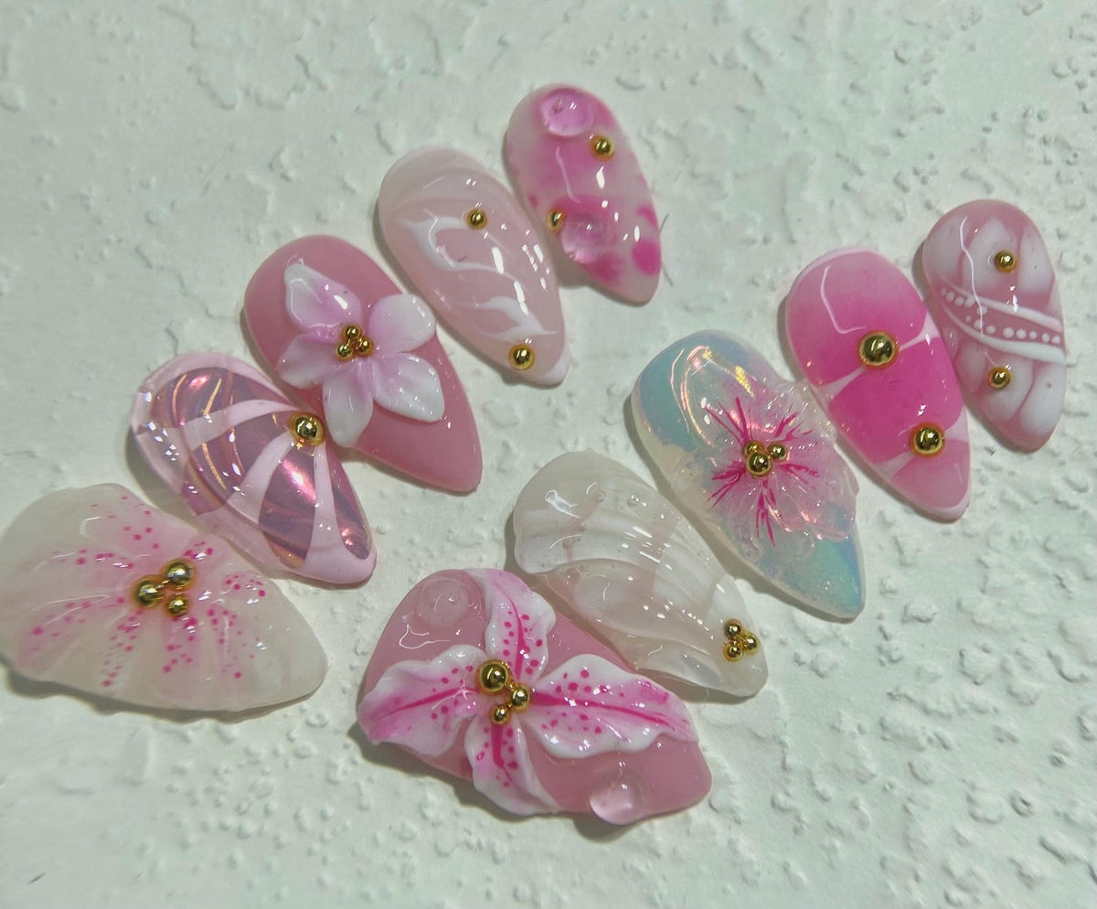 Set of ten pink and white artificial nails with gold accents. Each nail features a different floral design.