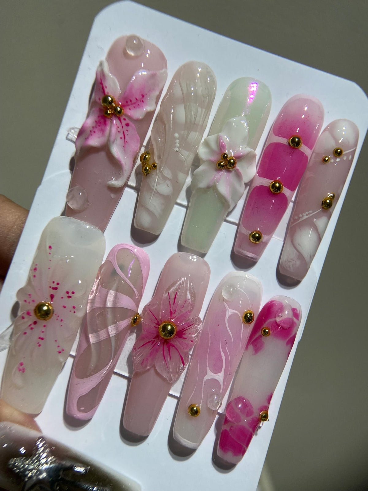 A set of 10 pink and white false nails with 3D flower designs and gold accents.