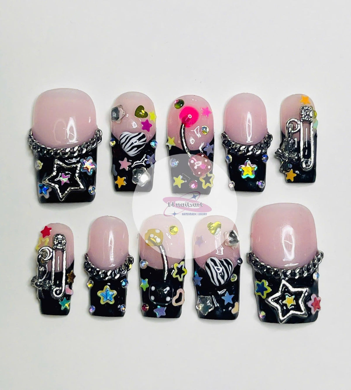 Ten black and pink press-on nails with various colorful designs, including stars, hearts, cherries, and a zebra print. Each nail has a silver chain detail.