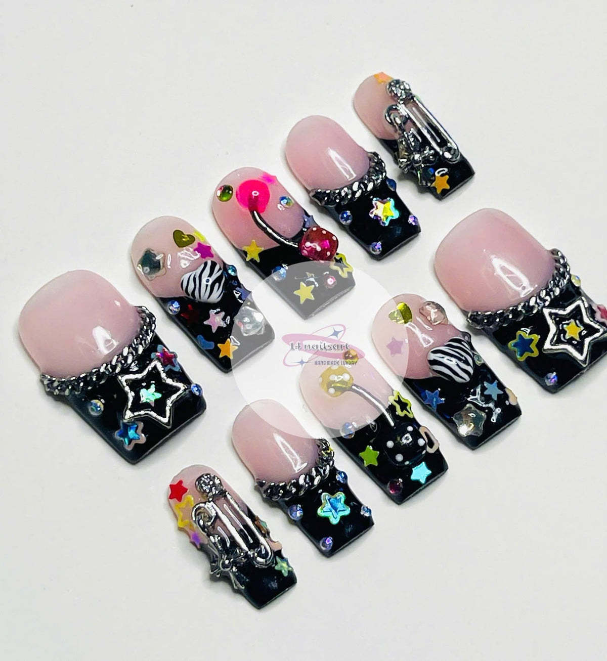 Set of ten pink and black press-on nails with various colorful embellishments, including stars, hearts, rhinestones, and a safety pin.