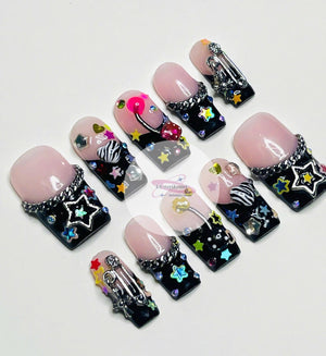 Set of ten pink and black press-on nails with various colorful embellishments, including stars, hearts, rhinestones, and a safety pin.