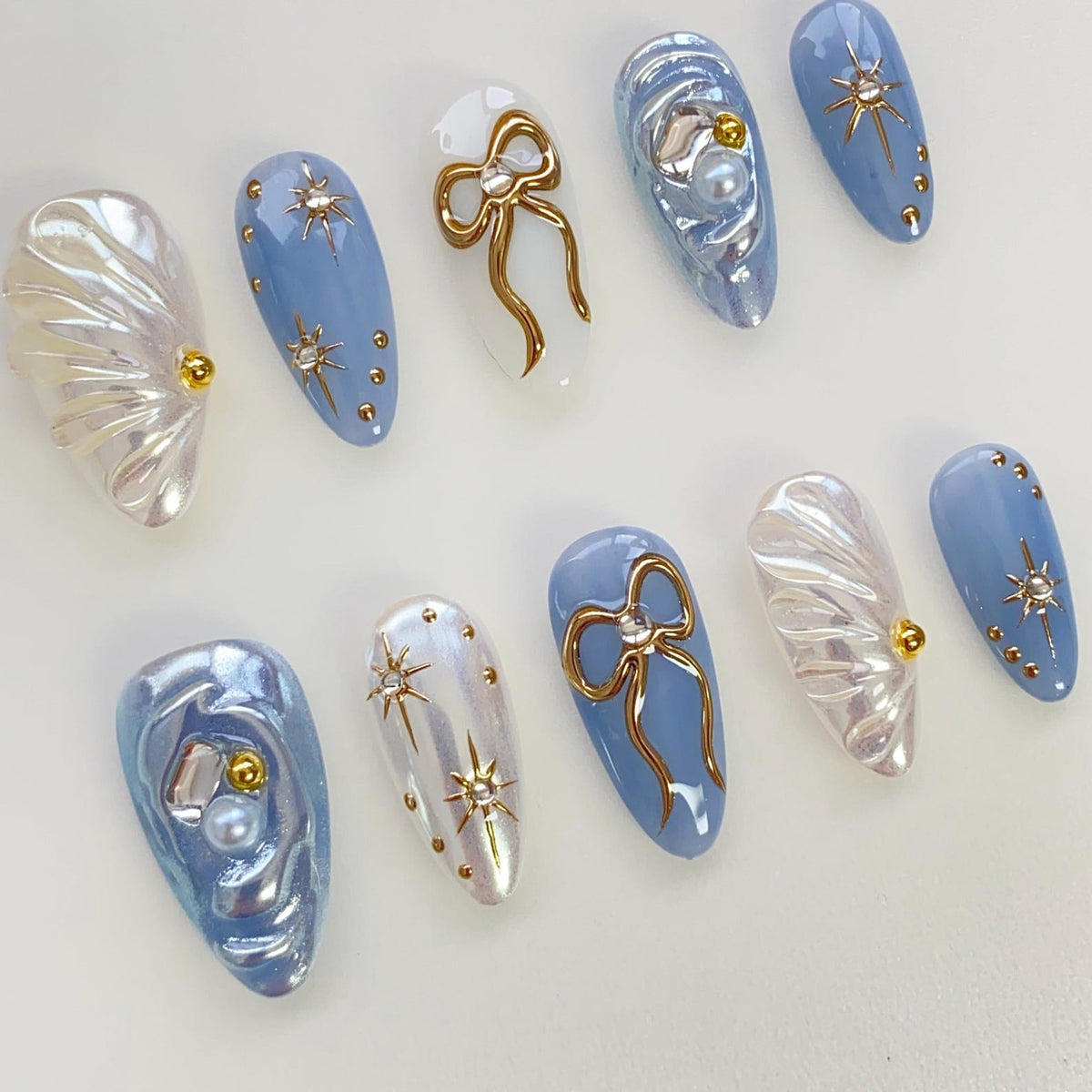 Set of ten blue and white false nails with various designs, including gold bows, stars, and pearl accents.