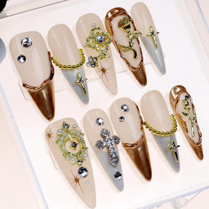 Set of ten long, almond-shaped, light pink and white false nails with gold accents. Each nail is decorated with a different design, including a rose, a cross, a chain, and pearls.